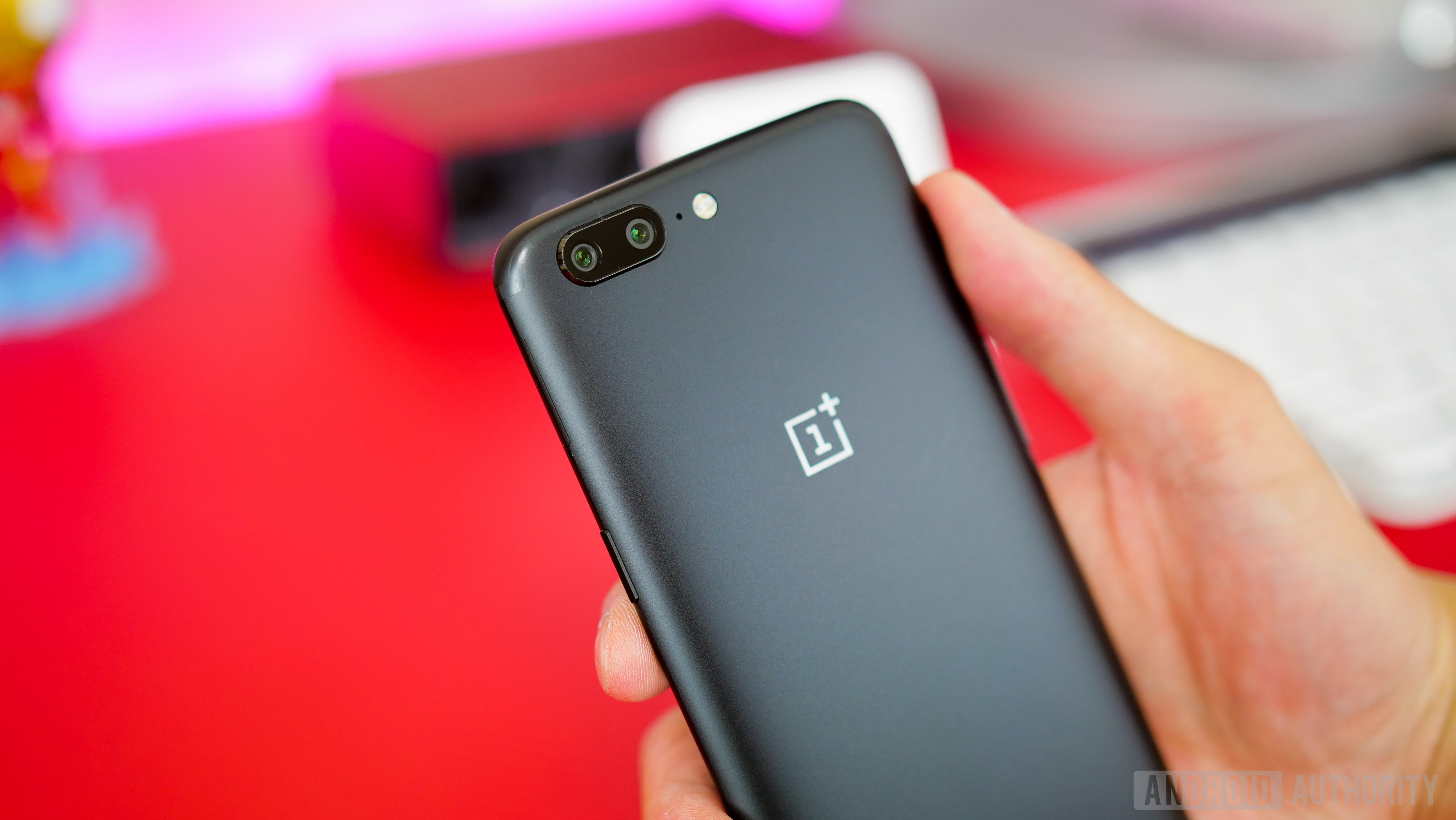 The OnePlus 5 in black, held in a person's hand, showing its rear cameras. 