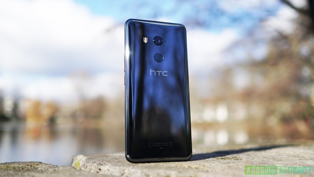 The HTC U11 Plus smartphone on a stone in front of a lake on a sunny day.