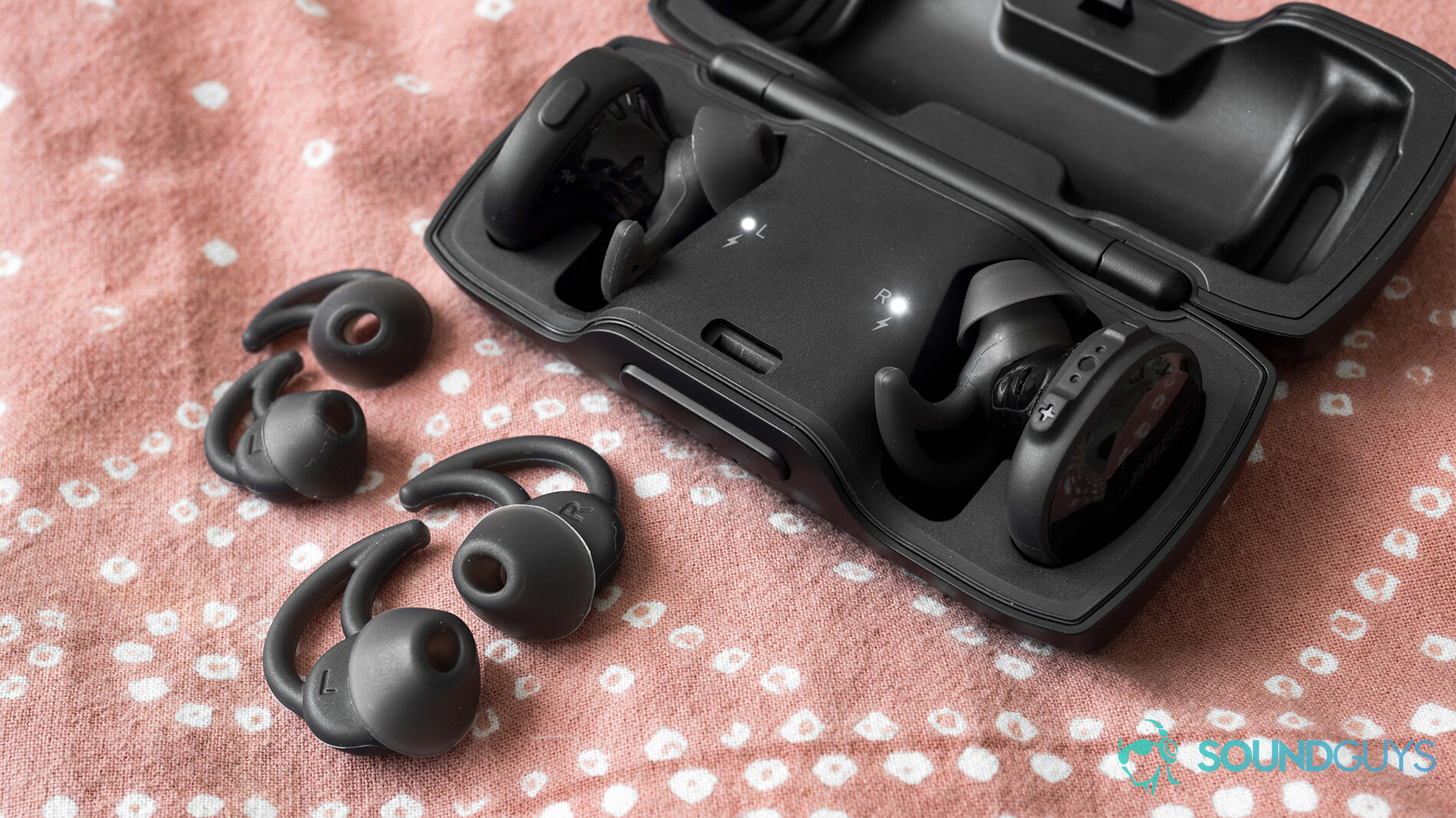 The Bose SoundSport Free in the case with the extra StayHear+ ear tips on a pink comforter.