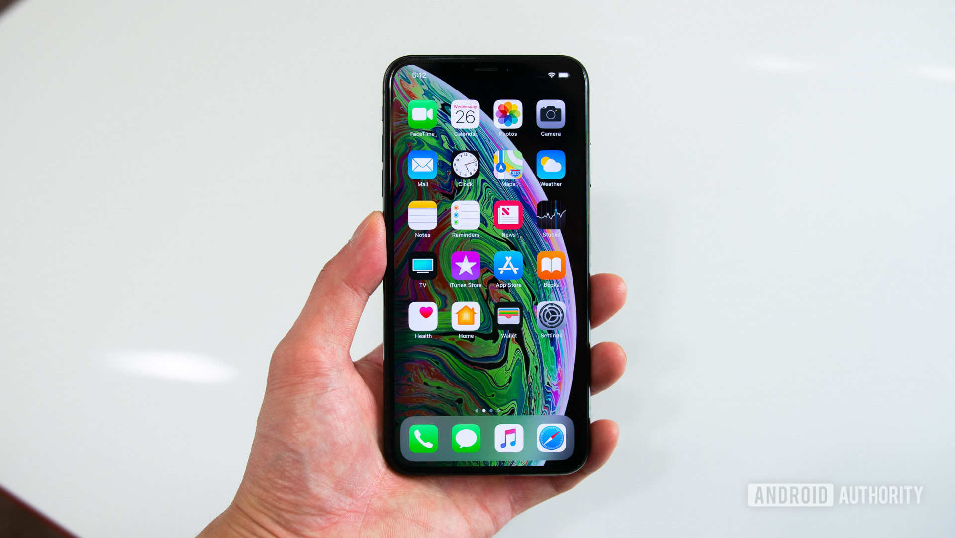 iPhone XS Max in man's hand against a white backdrop.