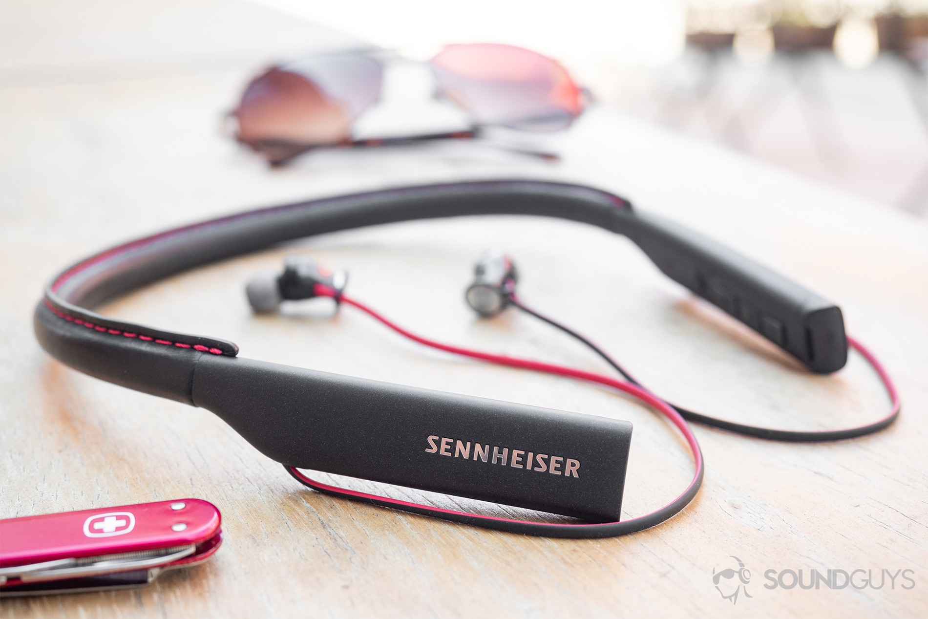 Are Beats worth it? Sennheiser HD1 In-Ear Wireless earbuds on a wooden table with a Swiss Army Knife in the foreground and sunglasses in the background.