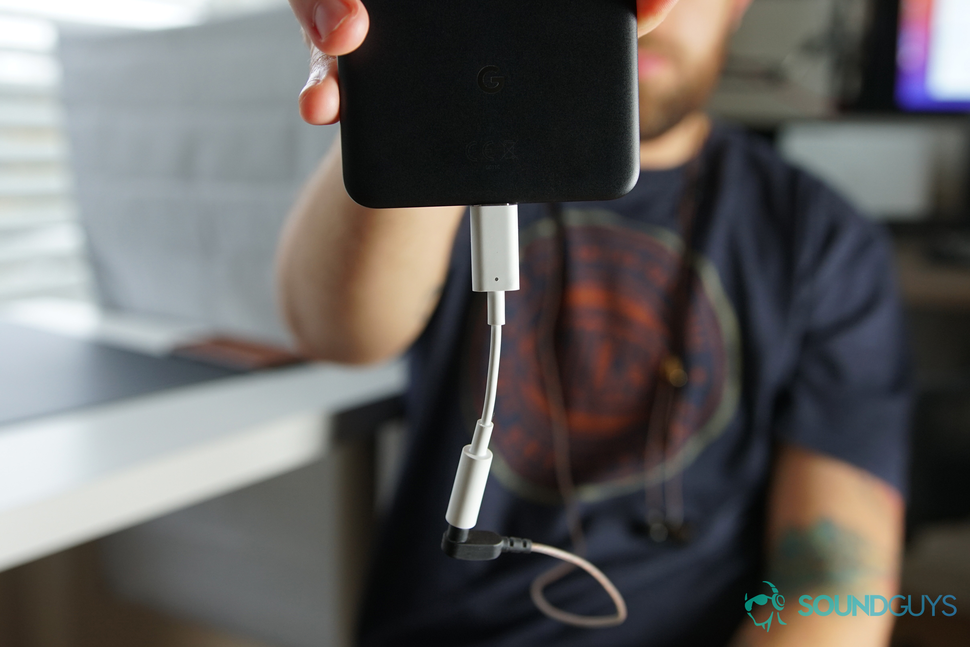 A man holding a phone with a Google Dongle in lieu of USB-C headphones.