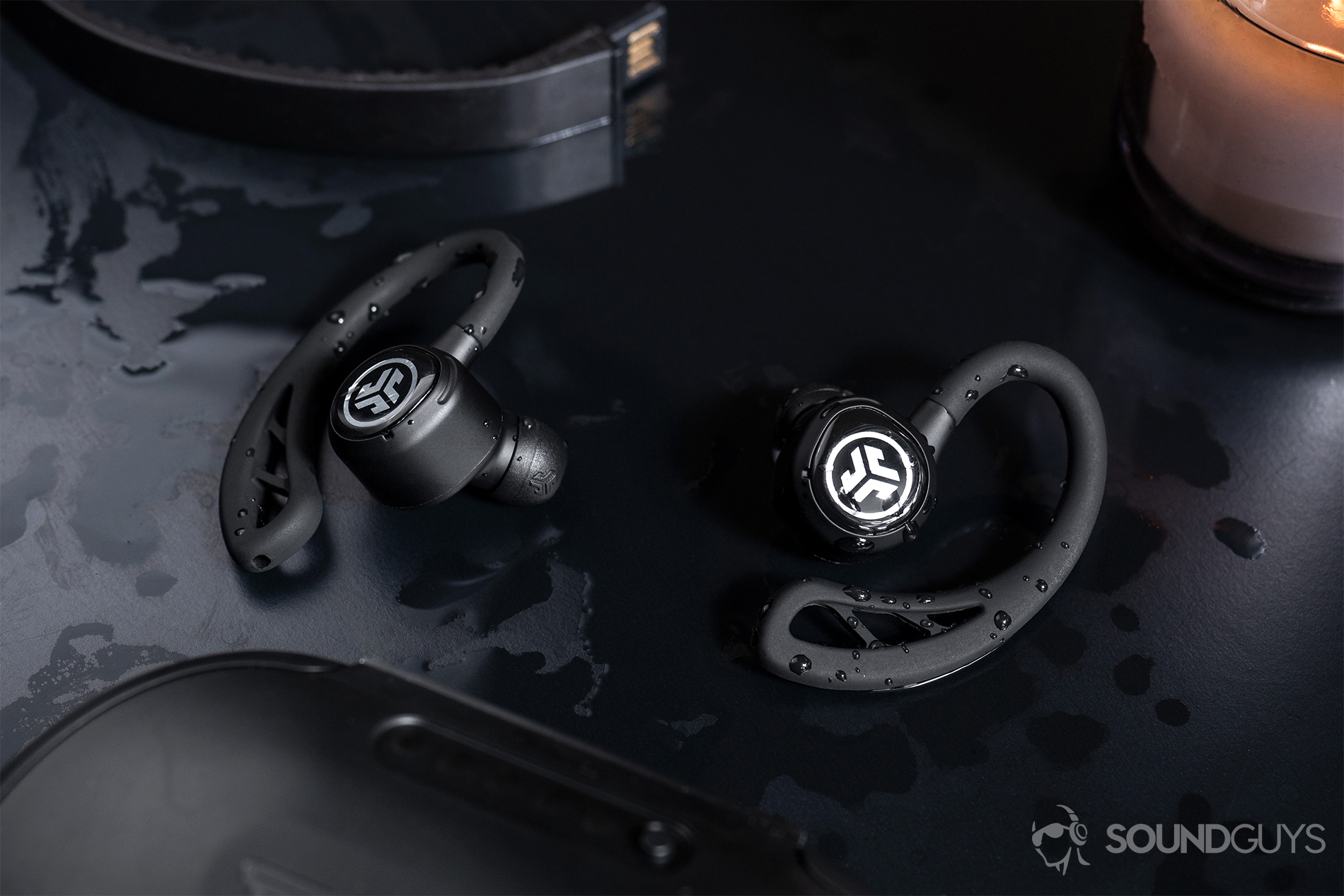 JLab Epic Air Elite: The earbuds surrounded by water on a black table.
