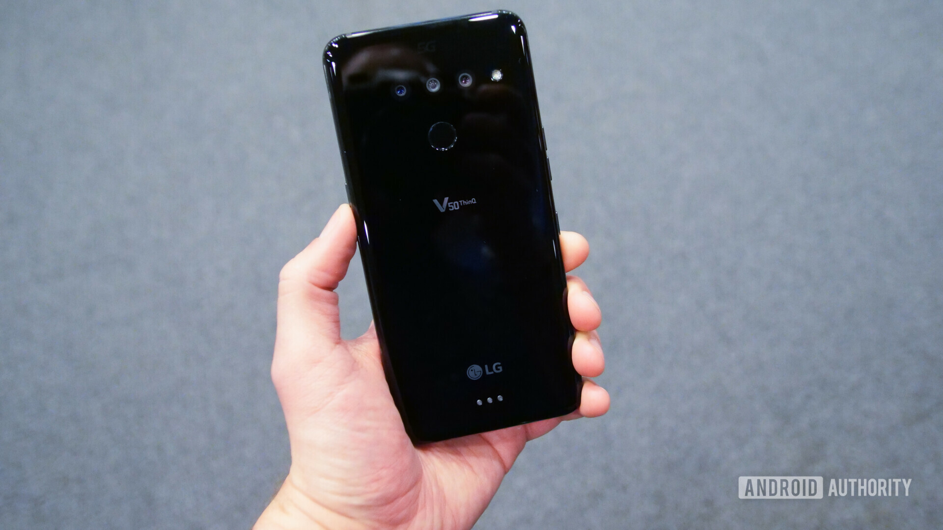 Backside photo of the LG V50 ThinQ showing the tripple cameras, held in a hand.