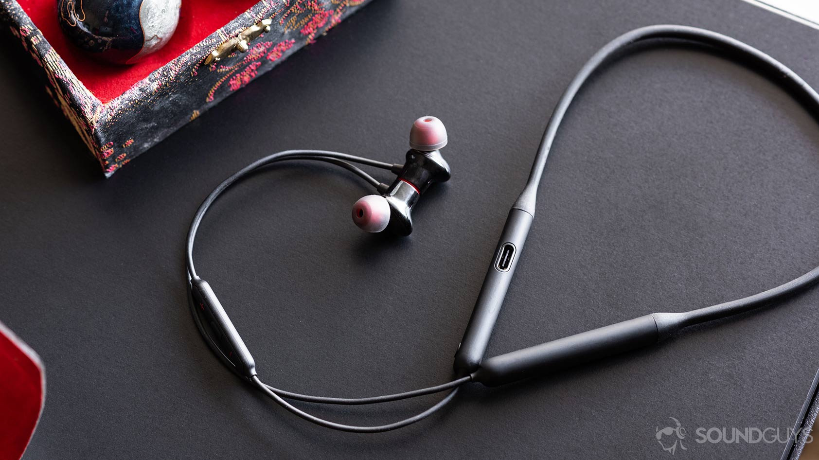 OnePlus Bullets Wireless 2: Full image of the earbuds and neckband with the cable curling up and around on a black table.