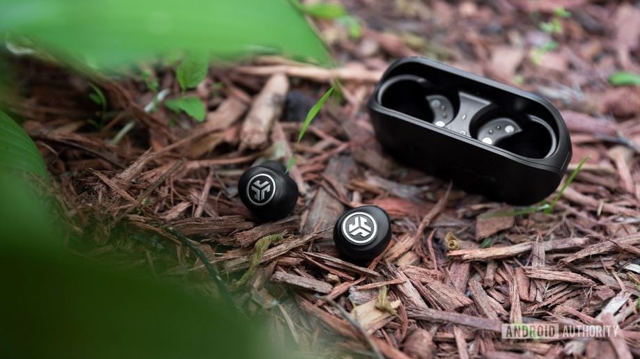 A photo of the JLab GO Air cheap true wireless earbuds with the earbuds outside of the case on a mulch pile, almost obscured by leaves in the foreground.