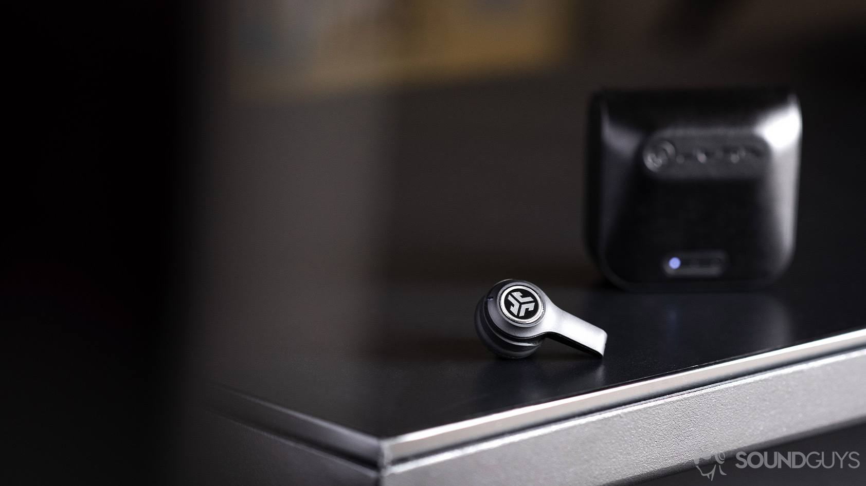 One JLab JBuds Air Executive earbud outside of the case, which is standing vertically.