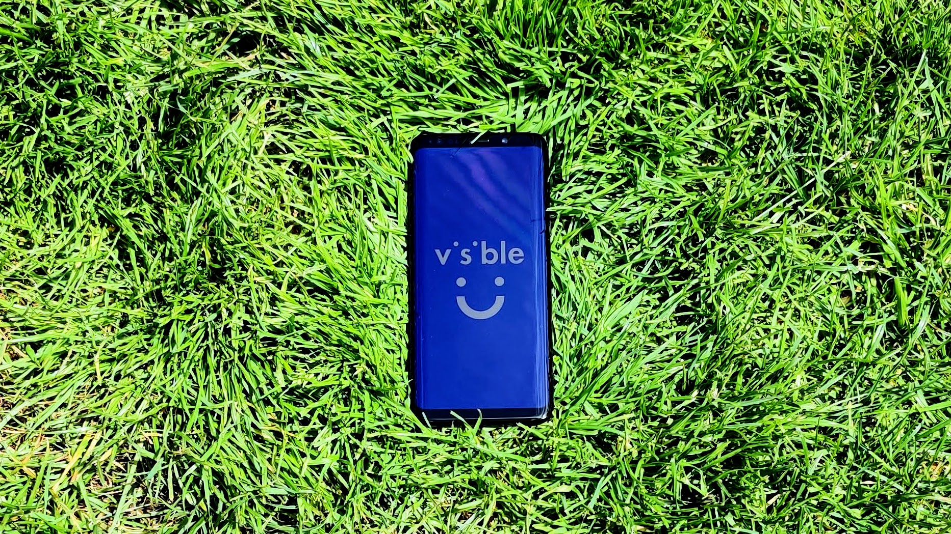 Un Samsung Galaxy S9 sur de l'herbe avec le logo Visible sur l'écran.