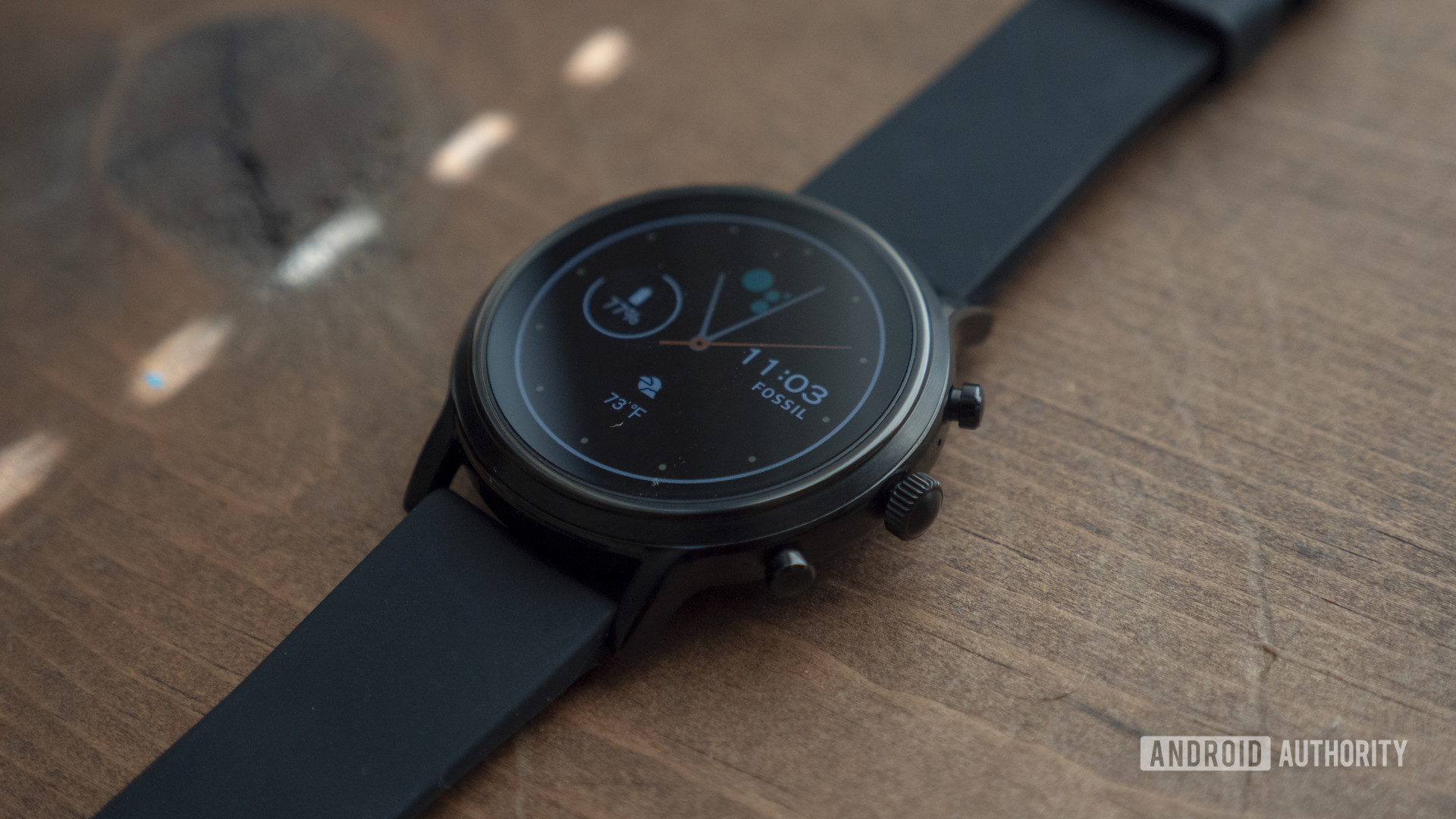A Fossil Gen 5 fashion smartwatch rests on a wooden surface displaying its watch face.