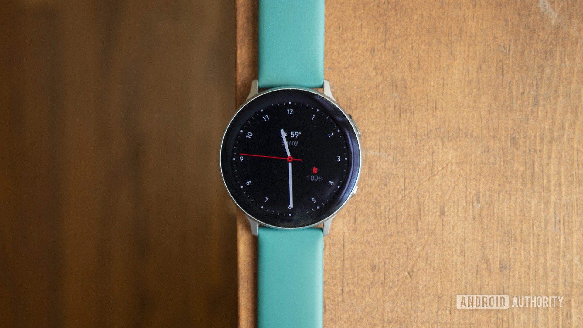 A samsung galaxy watch active 2 rests on a wooden surface displaying watch face.