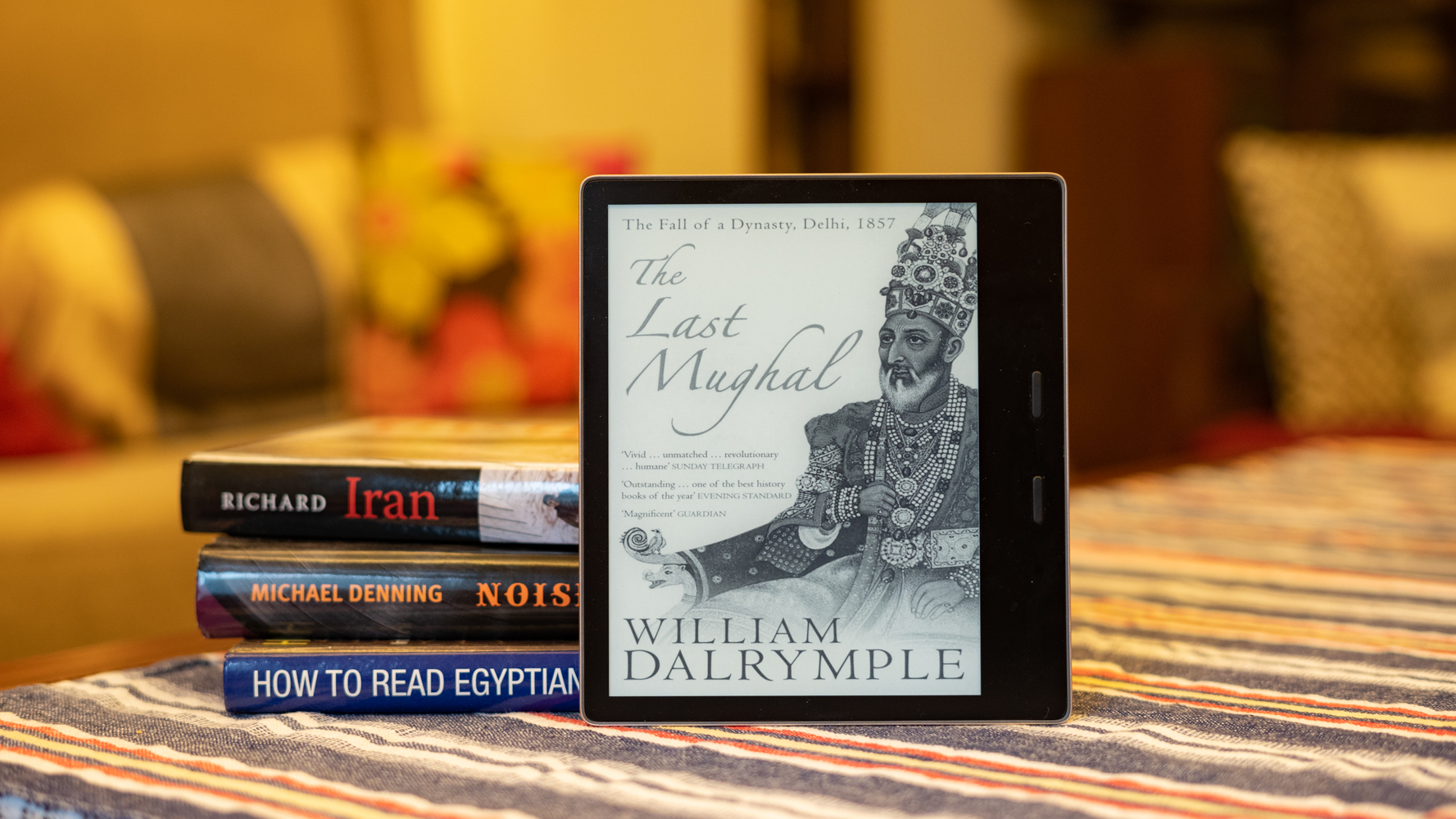Foto de perfil de Amazon Kindle Oasis que muestra The Last Mughal de William Dalrymple en la pantalla con una pila de libros en el fondo