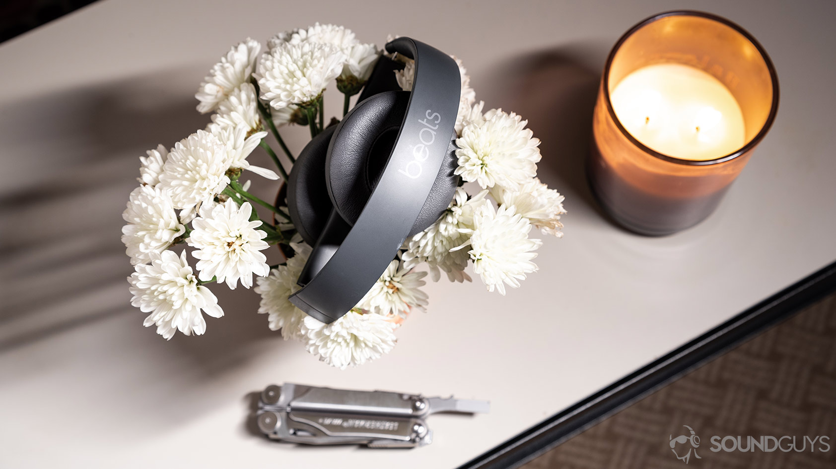 A picture of the Beats Solo3 Wireless headphones folded atop a bed of flowers with a candle and multitool.