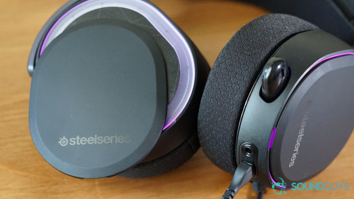 The SteelSeries Arctis Pro sits on a wooden table with its headphone plates coming off.