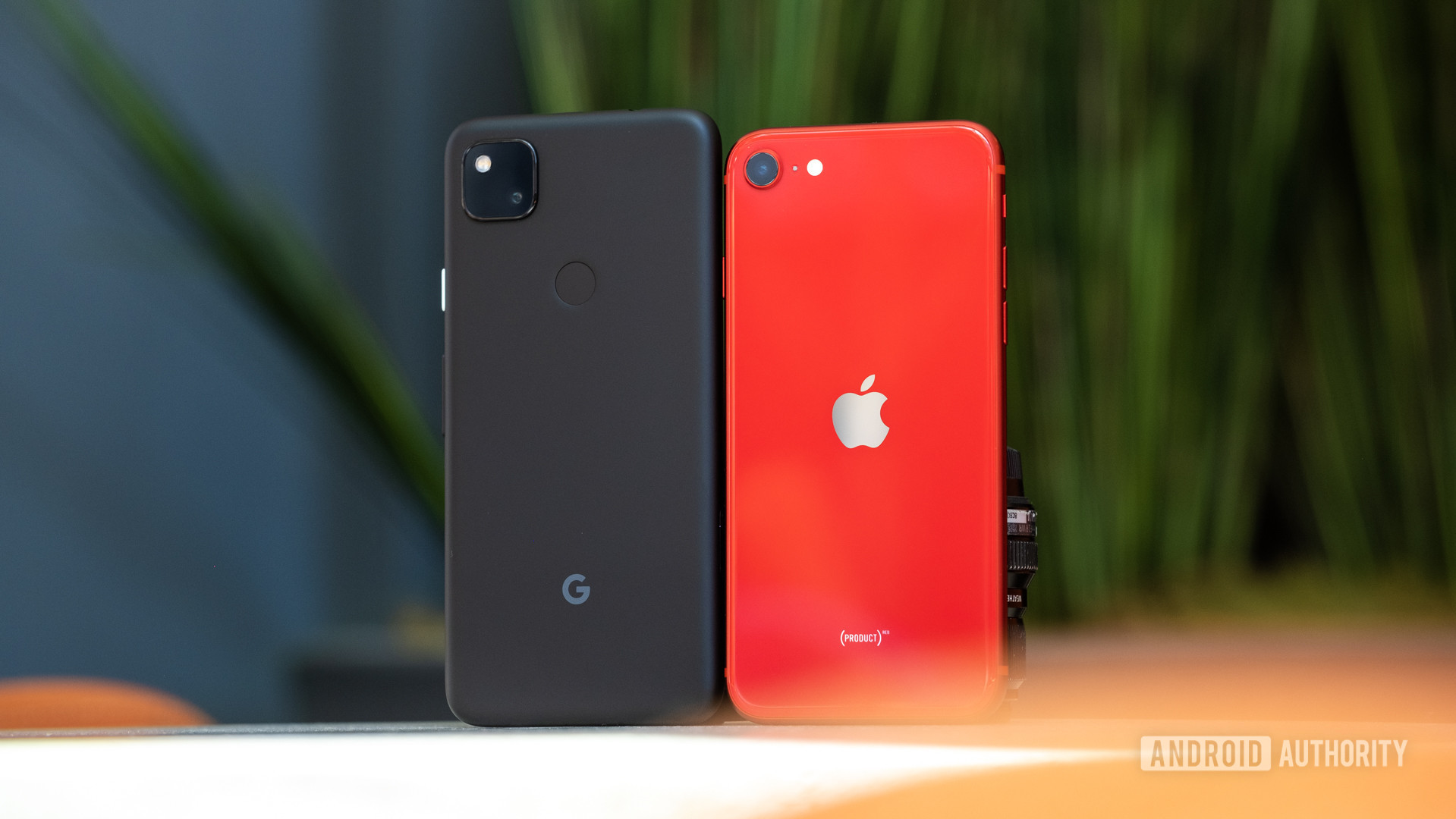 The Google Pixel 4a next to a red iPhone SE 2020 showing the back of both phones.
