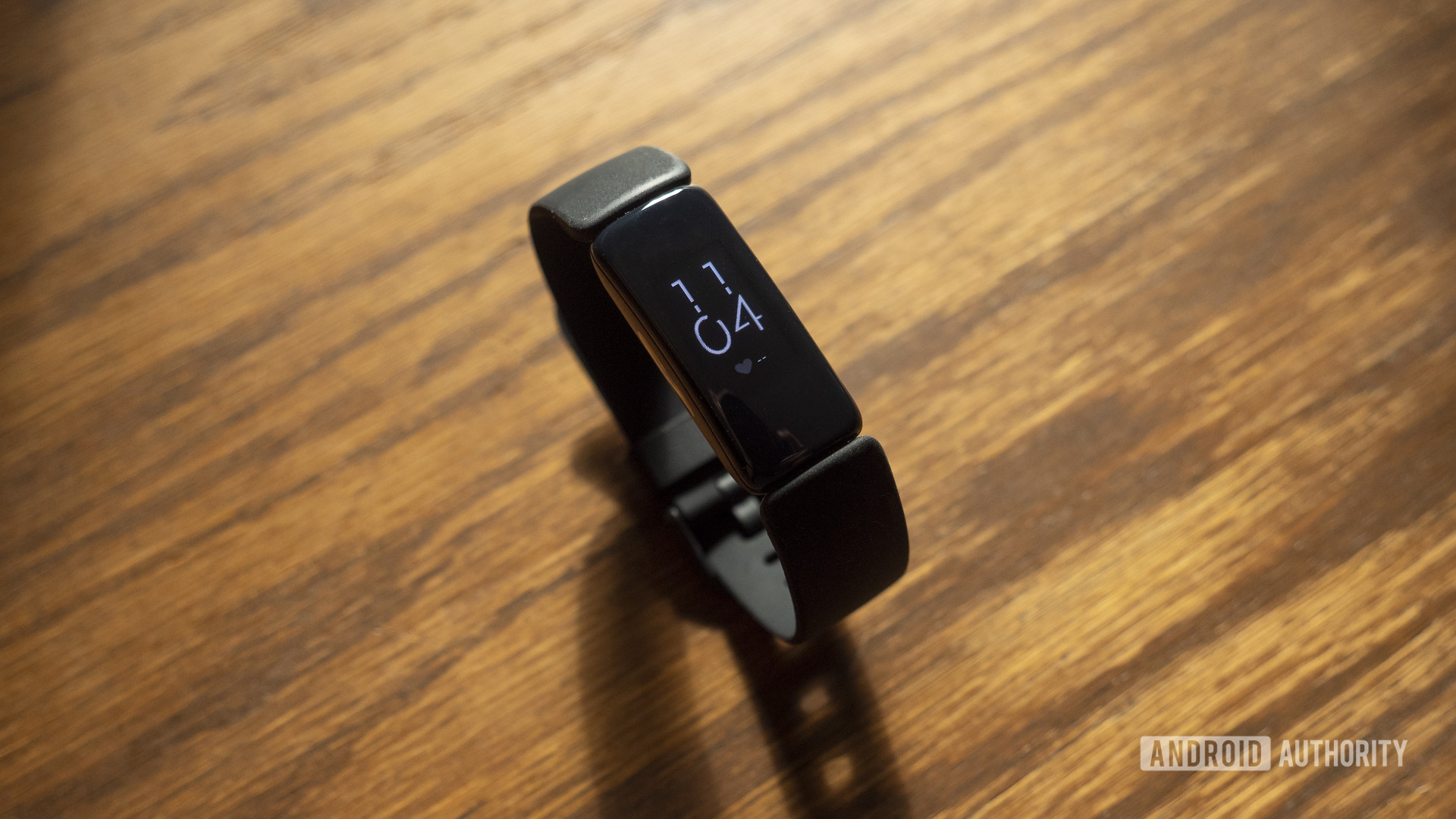 Un bracelet d'activité Fitbit Inspire 2 affiche l'heure tout en étant posé sur une table en bois.