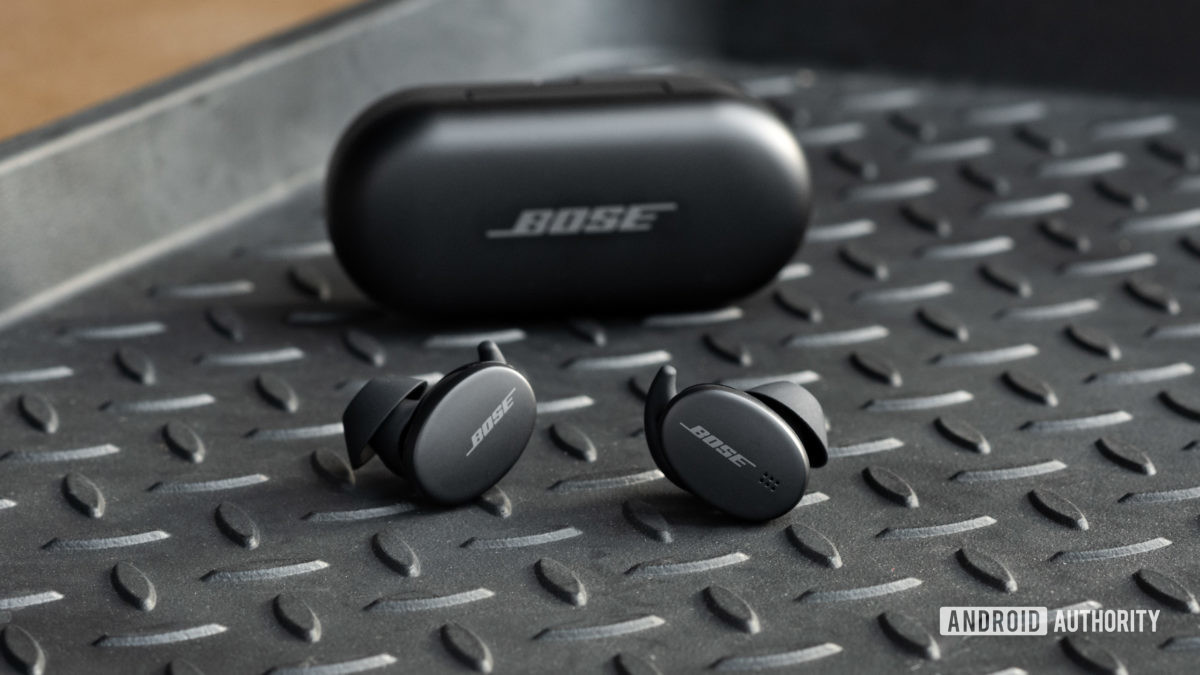 The Bose Sport Earbuds true wireless workout earbuds sit outside of the closed charging case, with the logos of the case and buds facing the viewer.