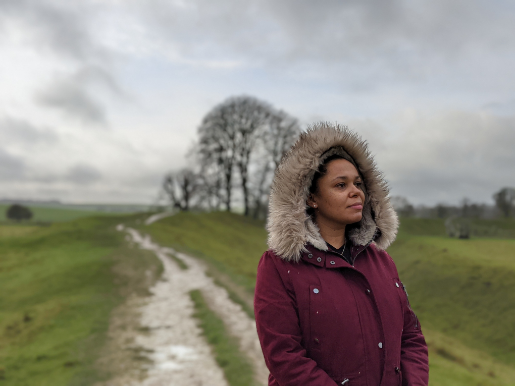 Portrait 1 Google Pixel 5 of a woman wearing a burgundy coat with a furry hood, in the countryside.