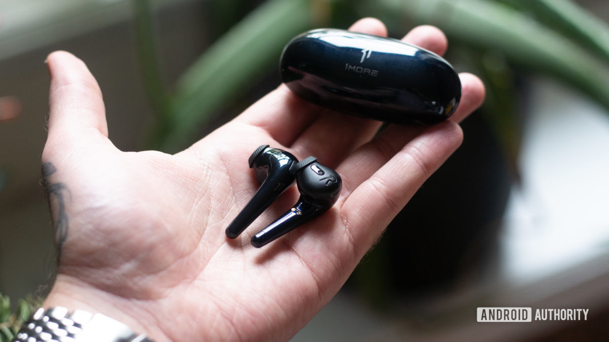A hand holds the 1MORE Comfobuds true wireless earphones and charging case.