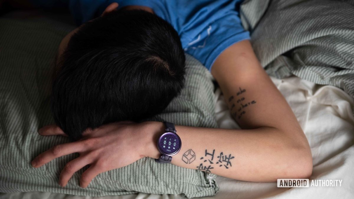 A woman sleeps in bed while she wears the Garmin Lily Sport Edition smart watch on her left wrist.