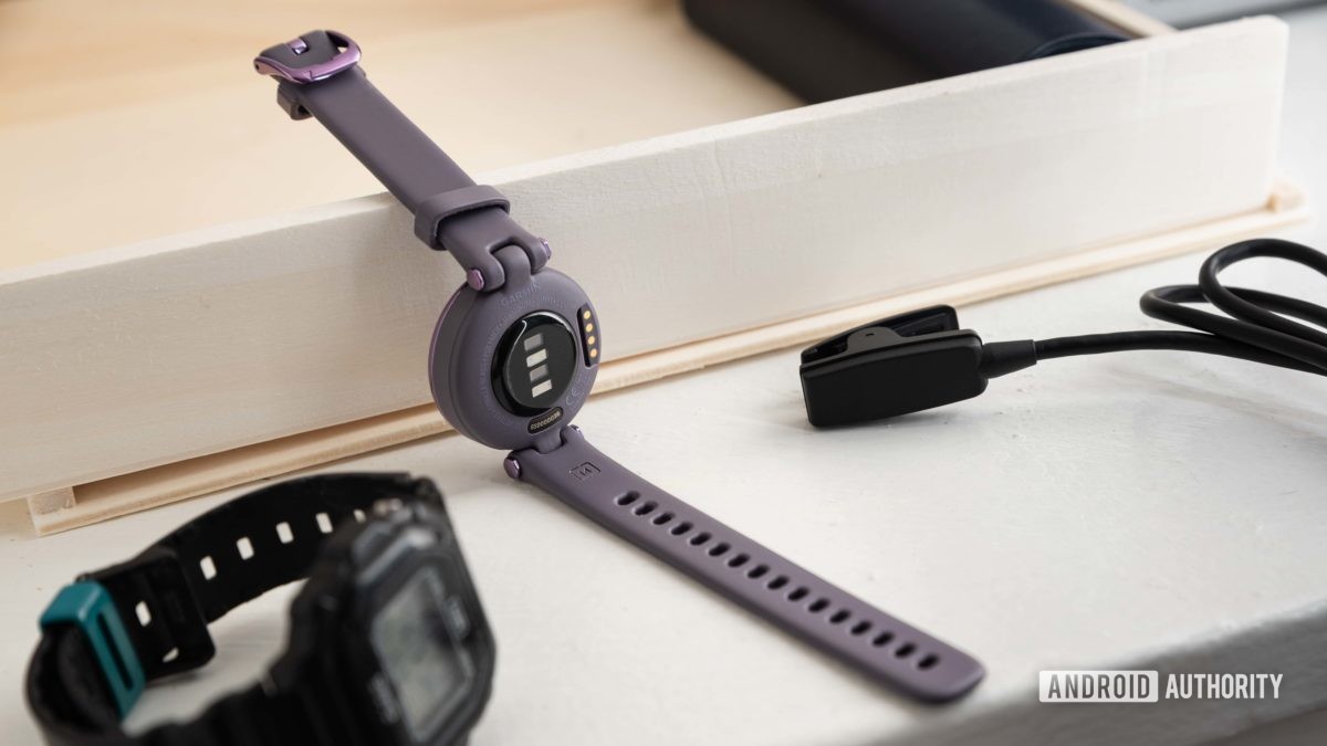 The Garmin Lily Sport Edition smart watch next to the proprietary charging cable and a Casio watch.