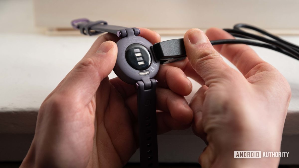 A woman connects the proprietary charging cable to the Garmin Lily Sport Edition smart watch.