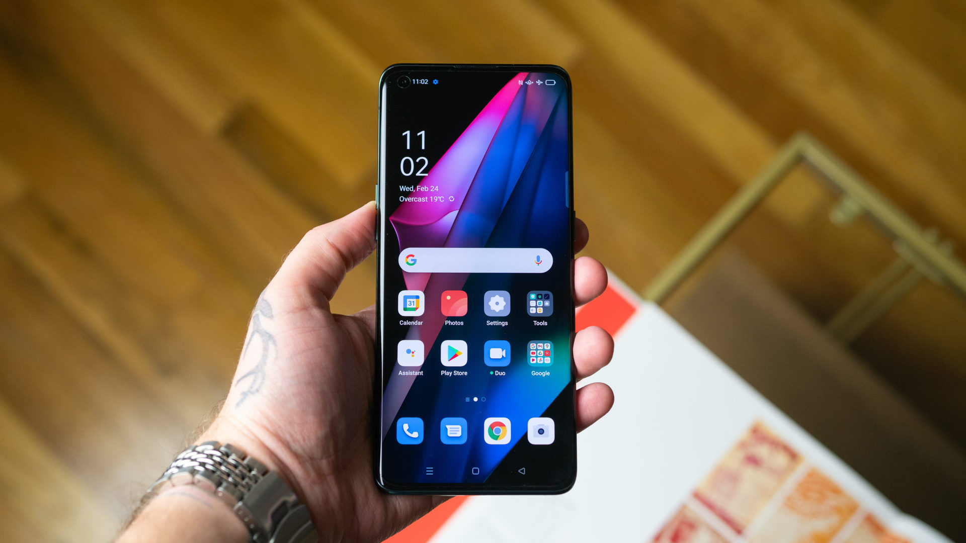 Oppo Find X3 Pro 5G in hand over a coffee table with the screen displaying the time and the apps. - The best dual SIM phones