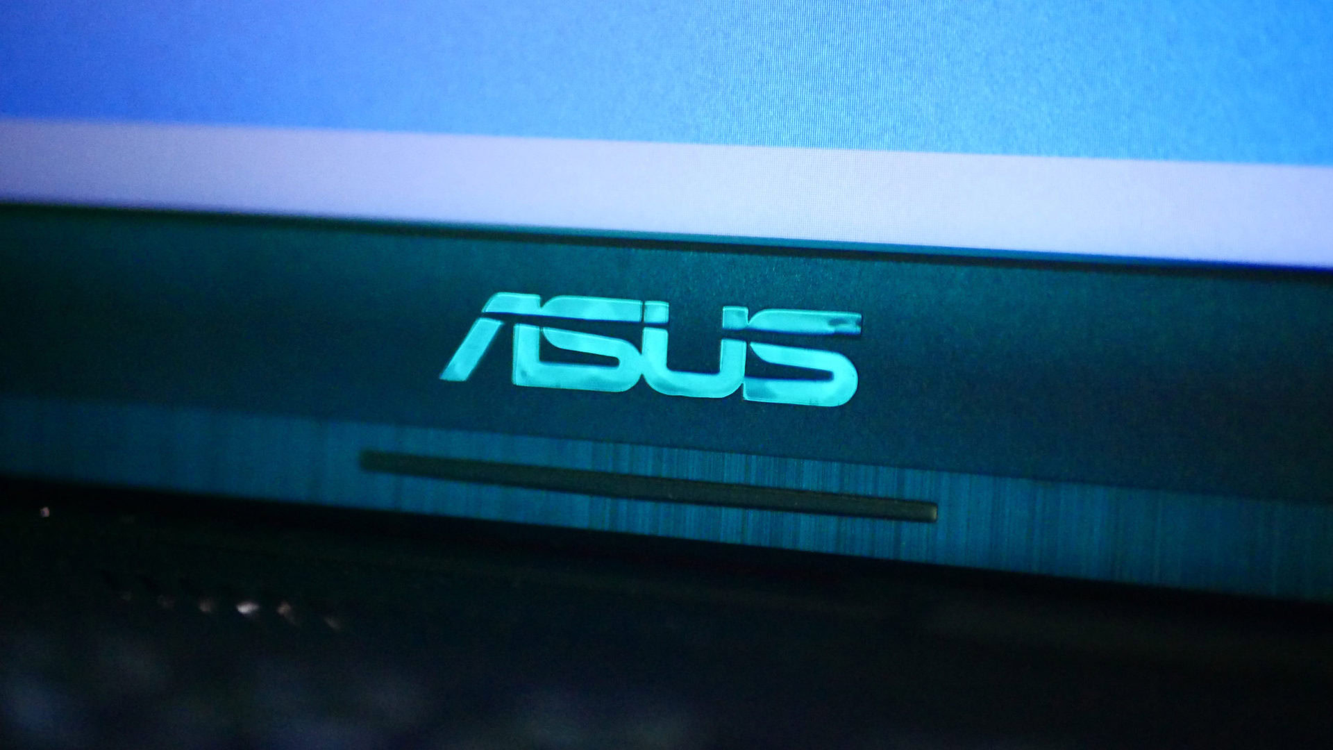 The Asus laptop logo photographed in teal lighting on an Asus TUF A17 laptop.