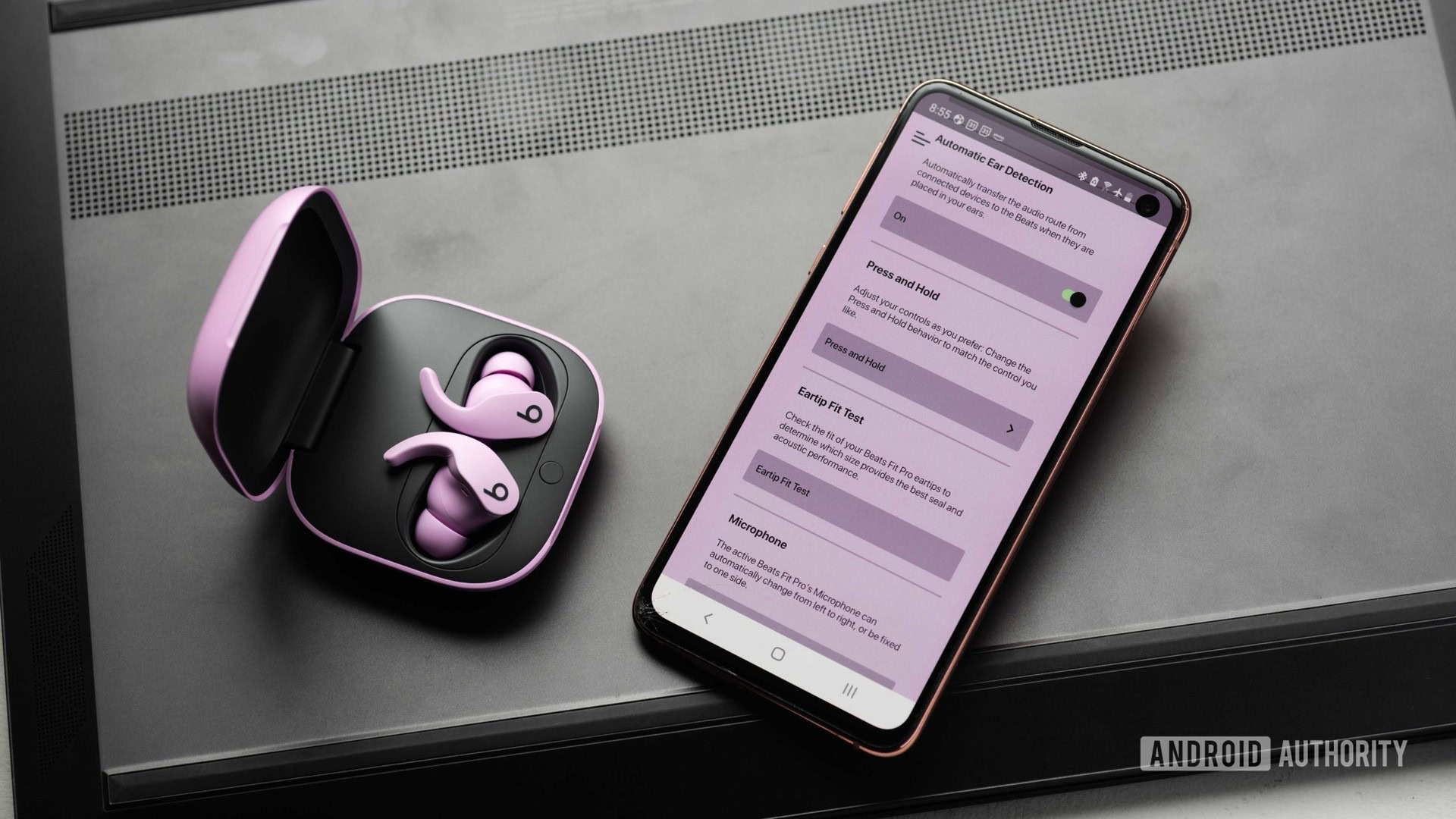 The Beats Fit Pro noise cancelling true wireless earbuds in the open charging case and next to a Samsung Galaxy S10e with the Beats app open. The app has a purple tint to it, presumably to match the earphones.