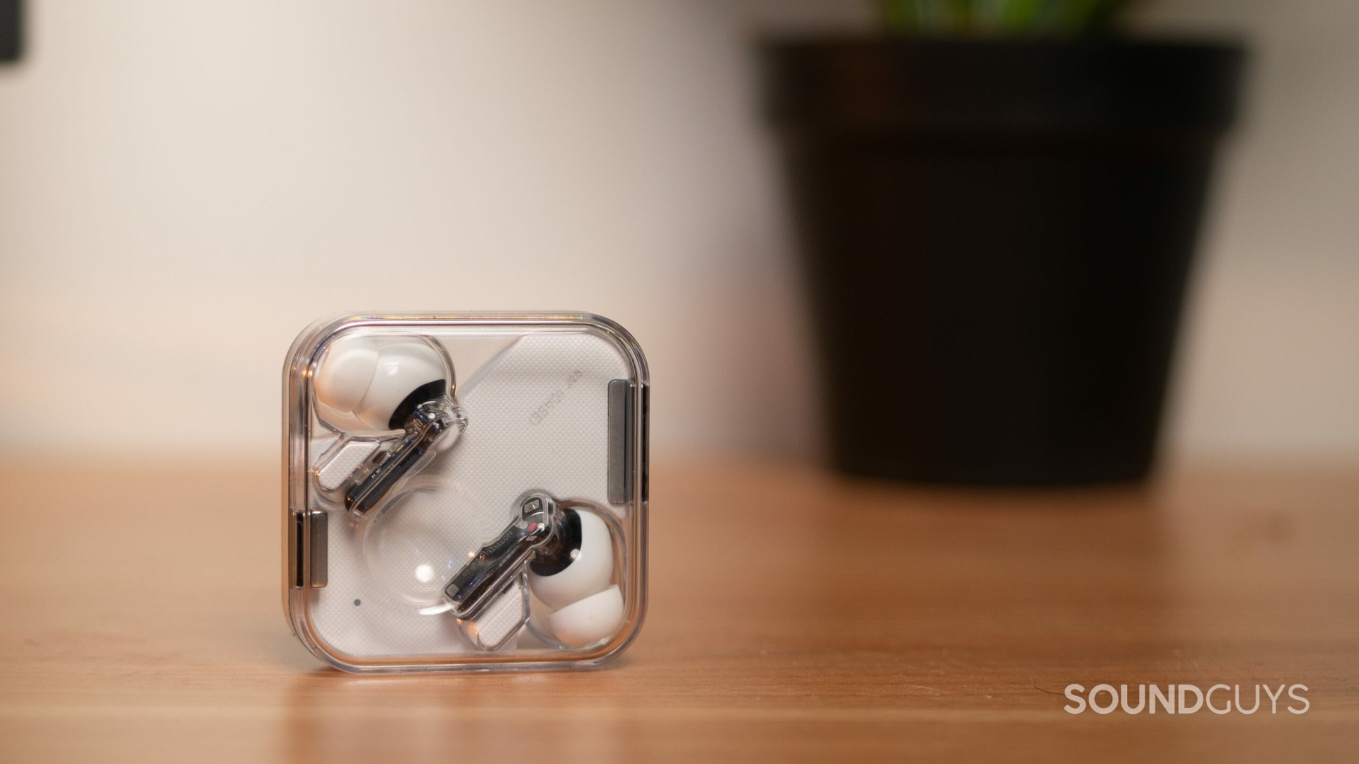 Les véritables écouteurs sans fil Nothing Ear 1 reposent dans le boîtier transparent car ils se tiennent debout sur une surface en bois.
