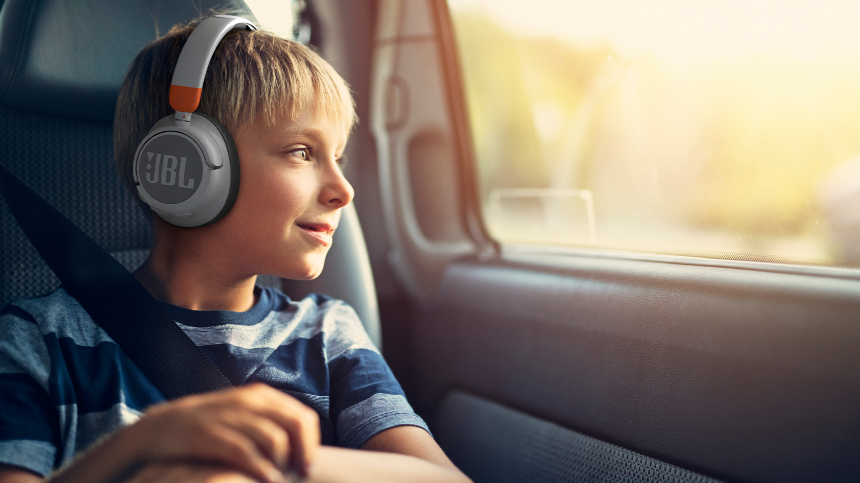 A young blonde child sits in a car while wearing the jbl jr460nc headphones in gray.
