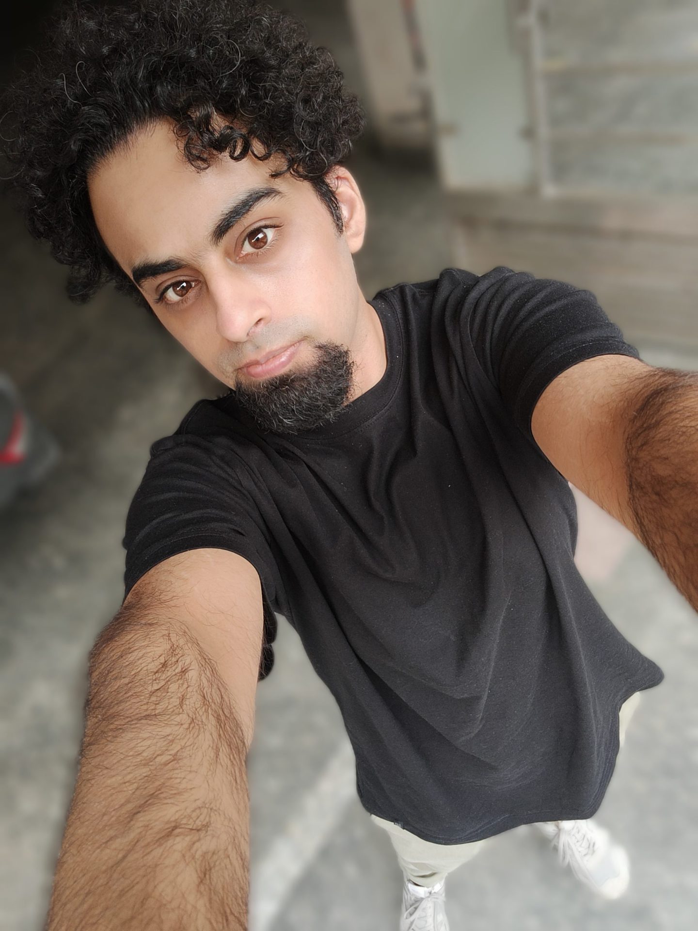 Realme GT selfie portrait mode shot of a man with dark curly hair and a beard, wearing a black t-shirt.