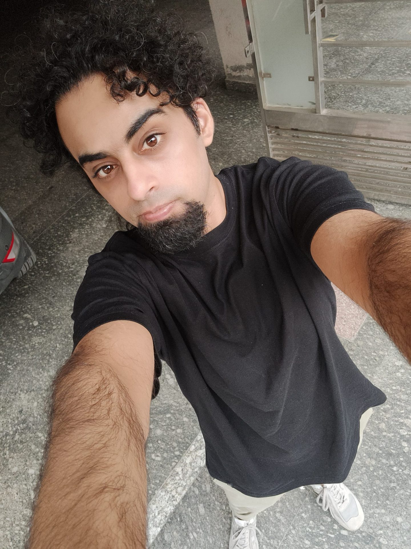 Realme GT selfie sample shot of a man with dark curly hair and a beard, wearing a black t-shirt.