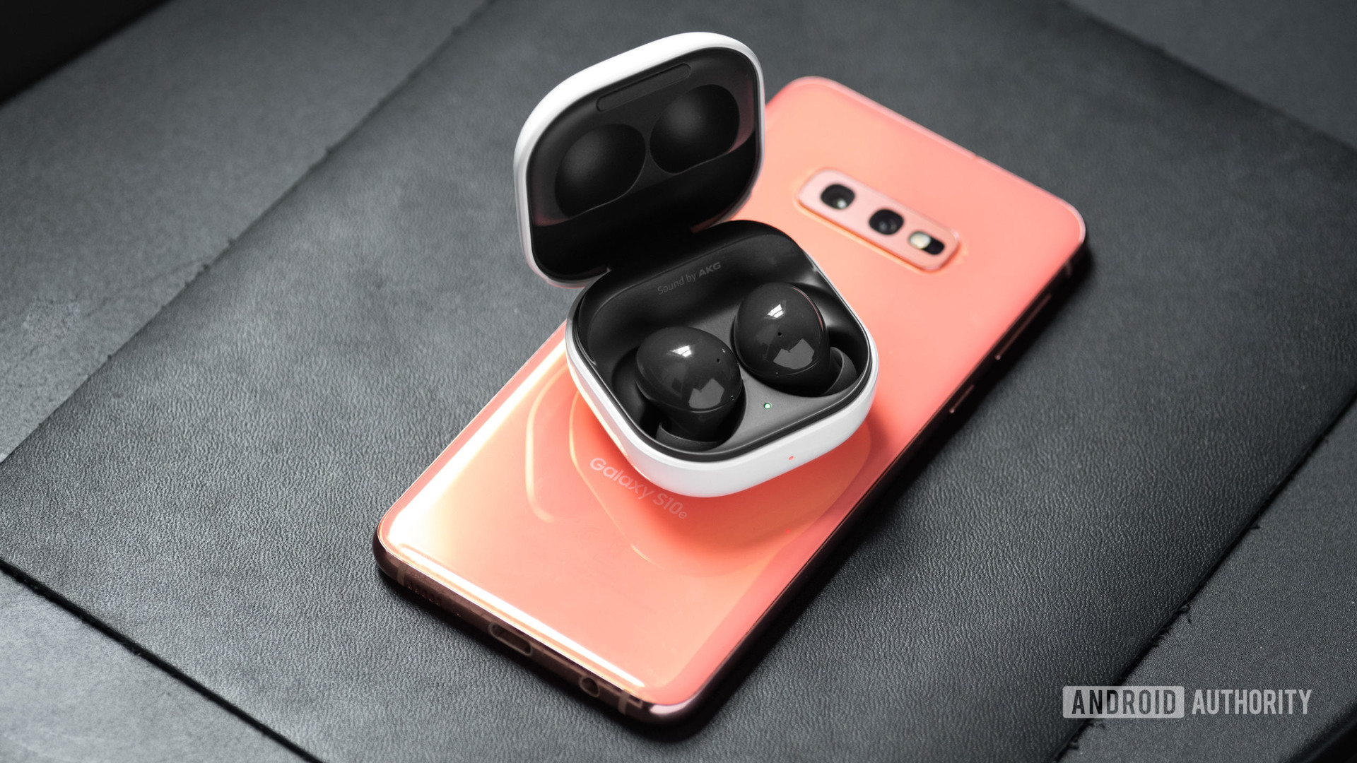 Les véritables écouteurs sans fil à réduction de bruit Samsung Galaxy Buds 2 dans l'étui de chargement ouvert au-dessus d'un smartphone Samsung Galaxy S10e en rose.