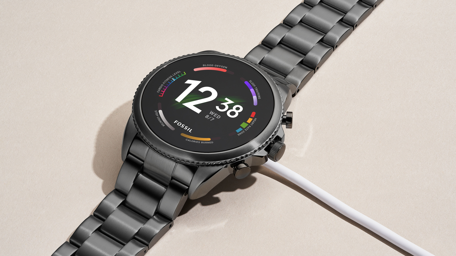 The Fossil Gen 6 smartwatch stainless steel on table with charger attached.