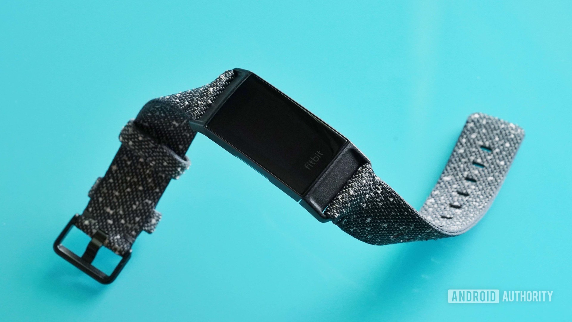 A Fitbit Charge 4 rests on a teal table.