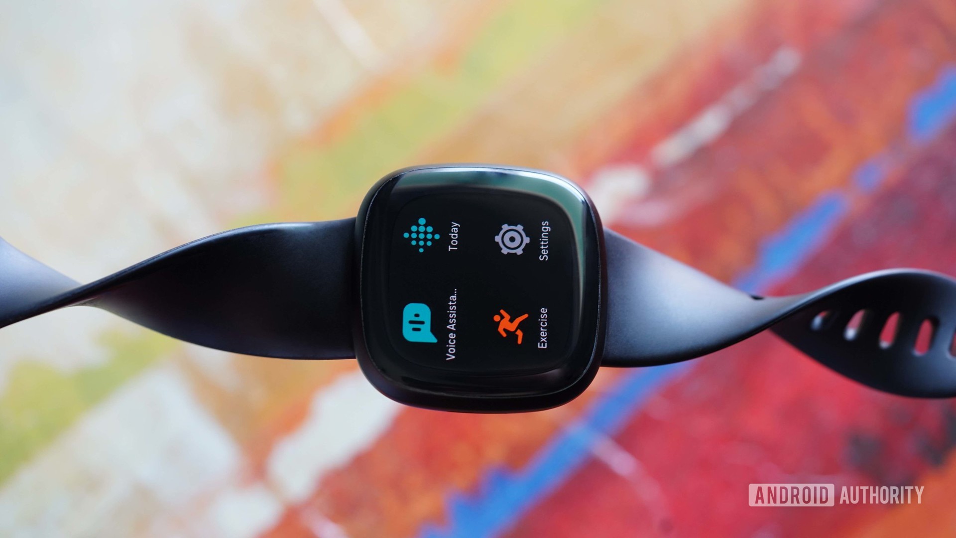 A Fitbit Versa 3 rests on an abstract, colorful background.