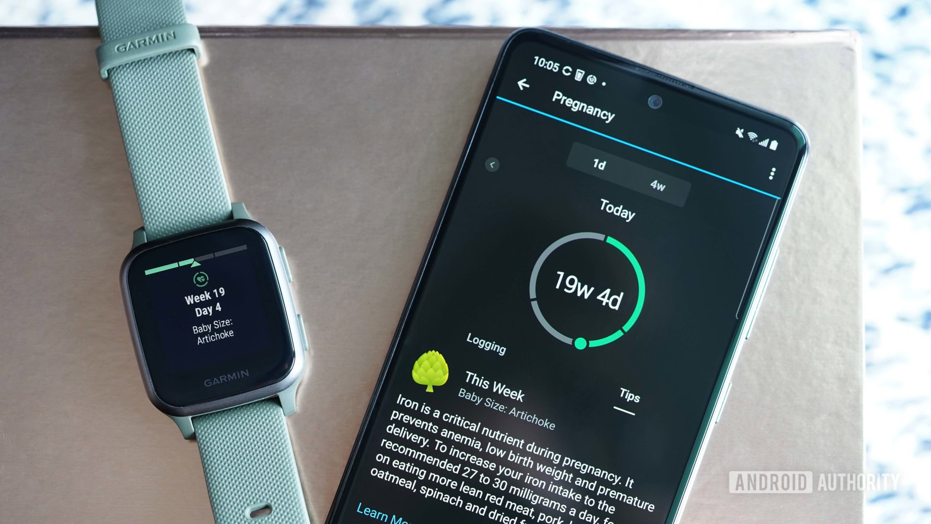 On a gold surface, a Garmin Venu Sq displays Pregnancy Tracking, alongside a paired Galaxy A51 open to the same feature in the Garmin Connect app.
