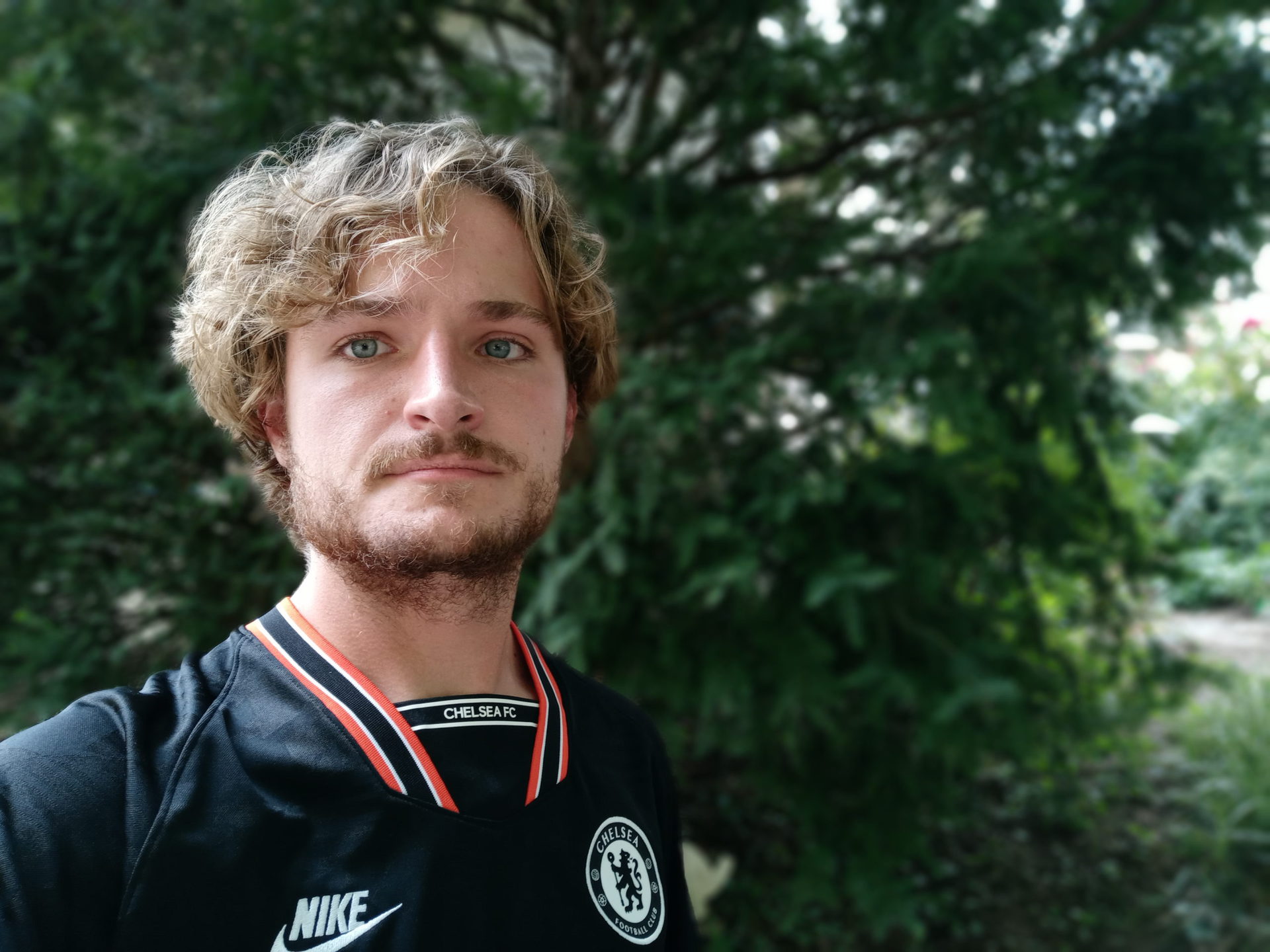 LG Stylo 6 portrait selfie of a man with blonde curly hair and facial hair, wearing a dark coloured top.