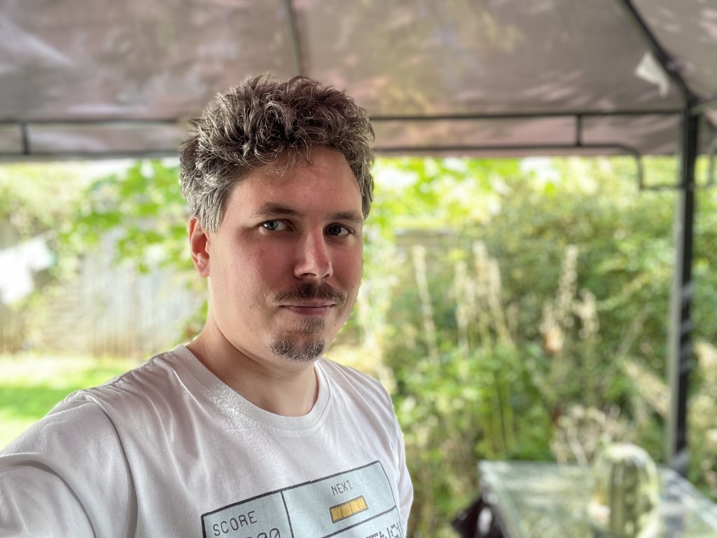 iPhone 13 Pro Max camera sample portrait HDR outdoors of a man with light curly hair and facial hair wearing a white t-shirt