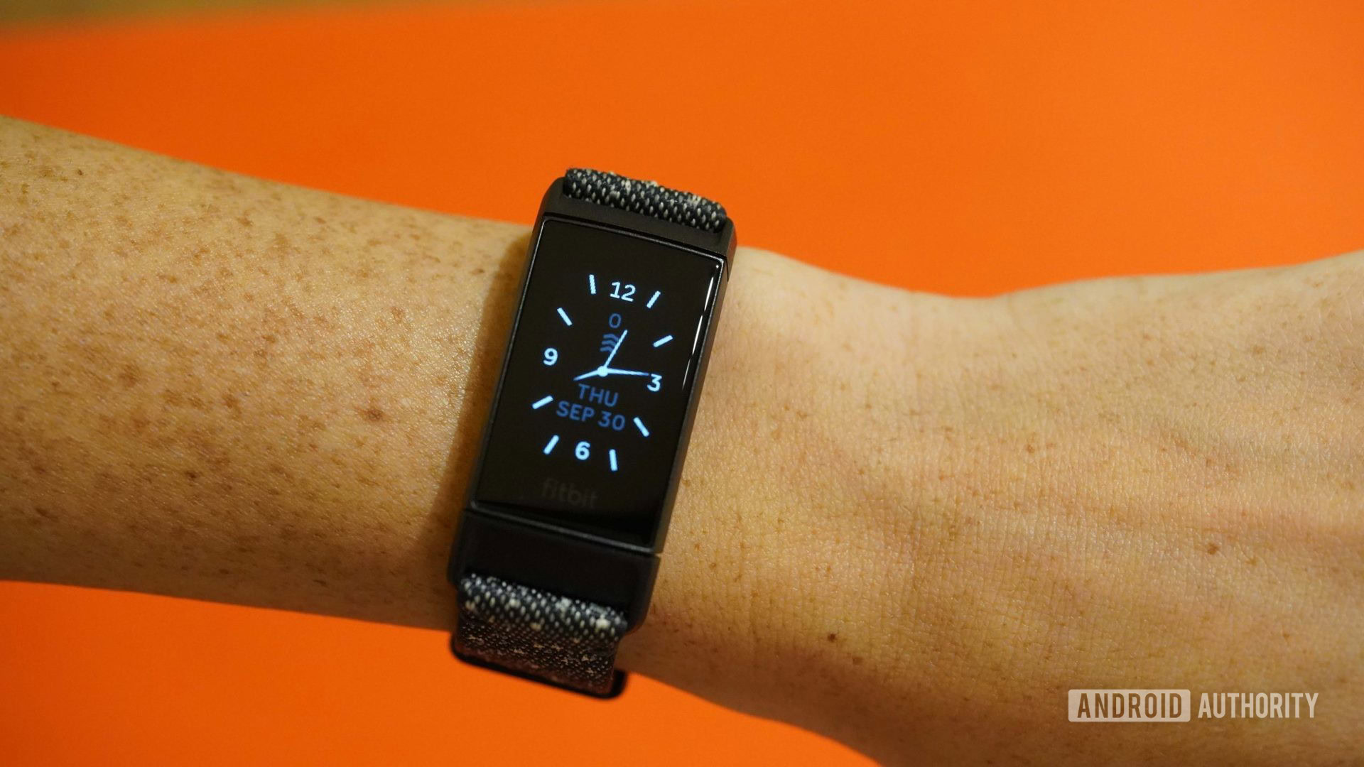 Un Fitbit Charge 4 affiche le cadran d'une horloge sur un fond orange