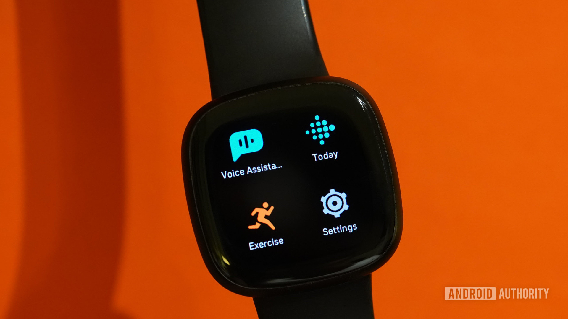 Une Fitbit Versa 3 affiche les applications devant un fond orange.