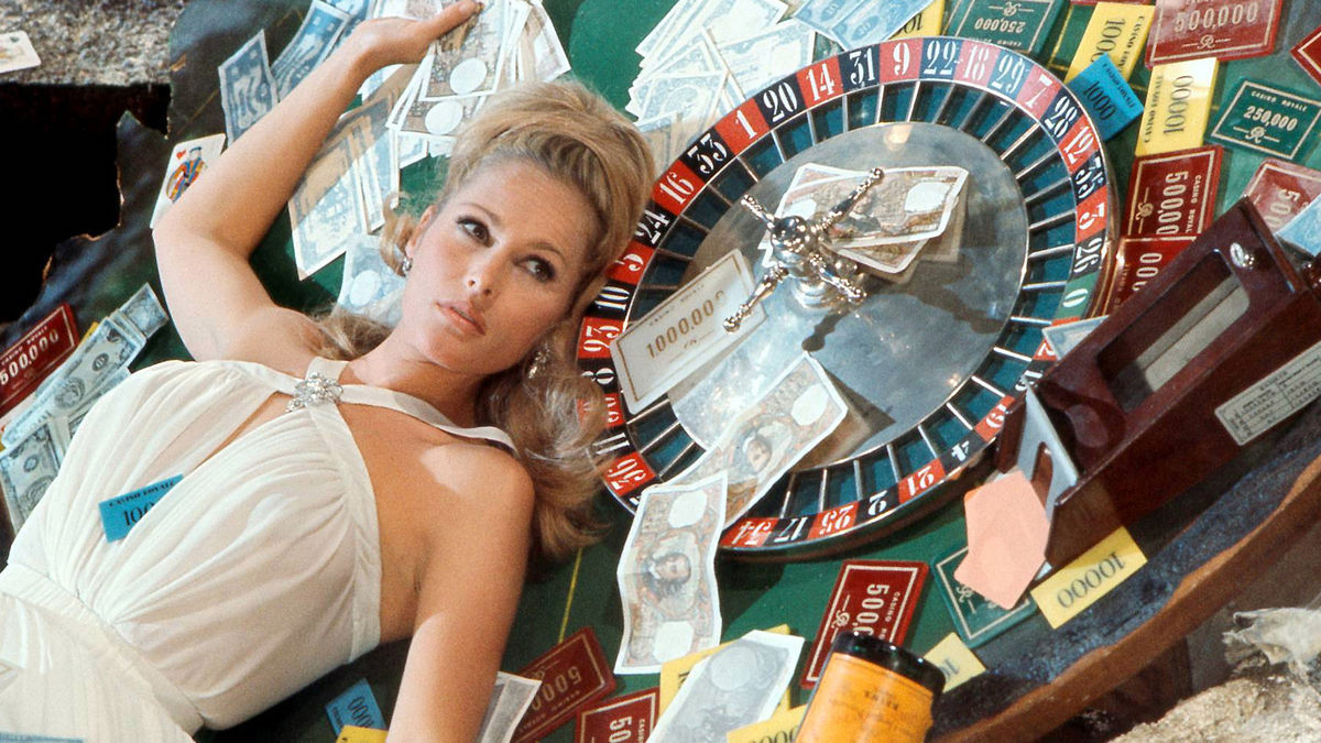 Casino Royale 1967 photo of a blonde Bond girl in a white dress, lying on a roulette table.