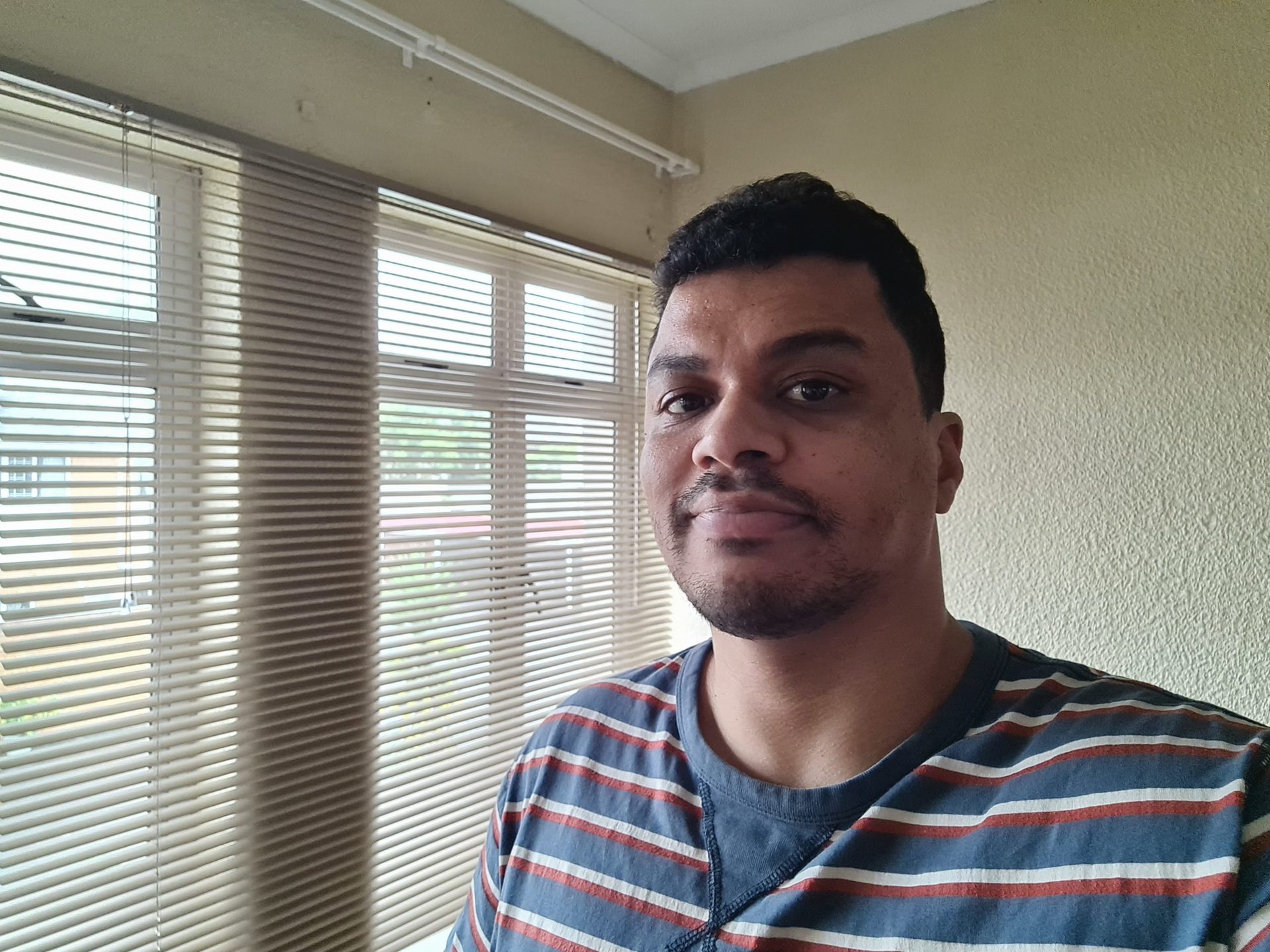 Galaxy S20 FE indoor selfie of a man with dark hair standing in front of a window and wearing a striped t-shirt