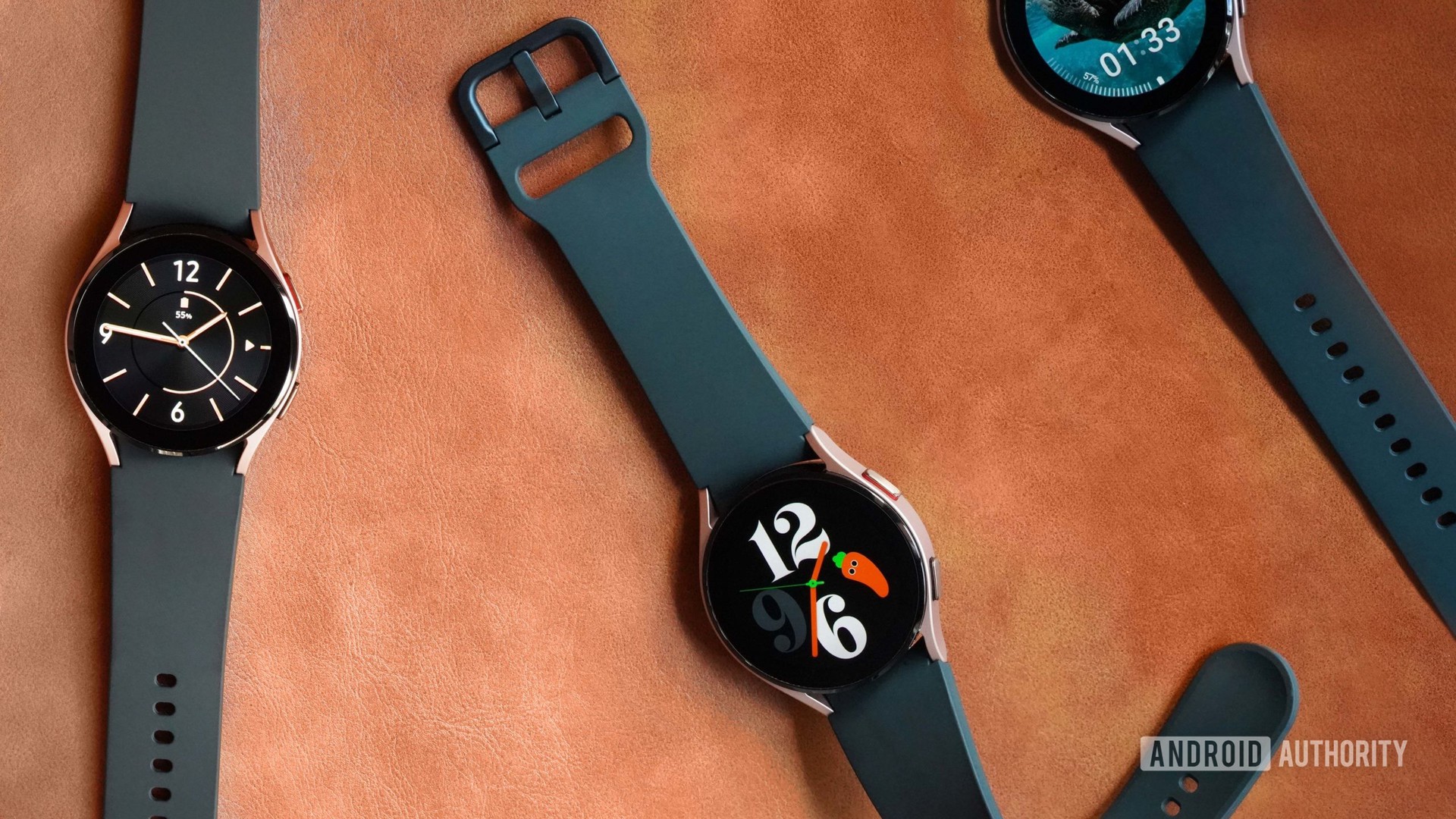 Three Samsung Galaxy Watch 4s rest on a leather surface displaying custom faces.