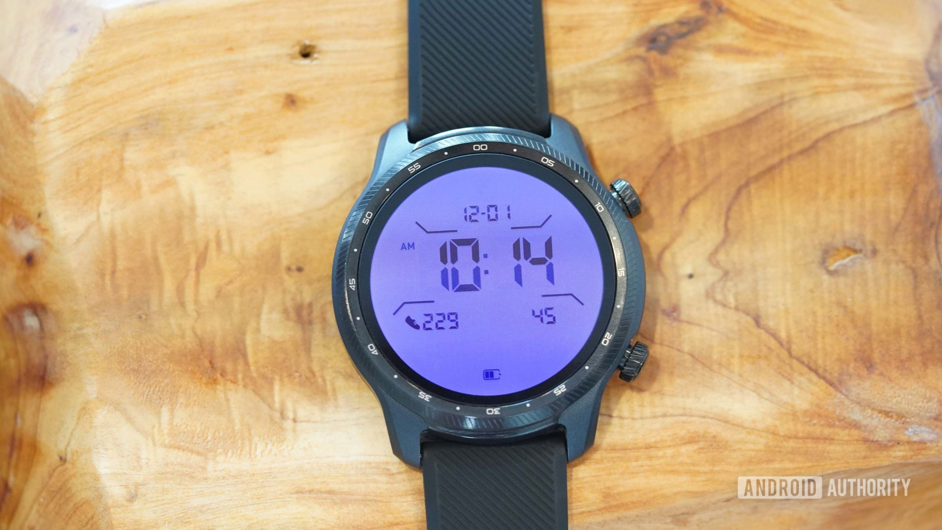 A TicWatch Pro 3 Ultra rests on a wooden surface with the customizable backlight shining in purple.