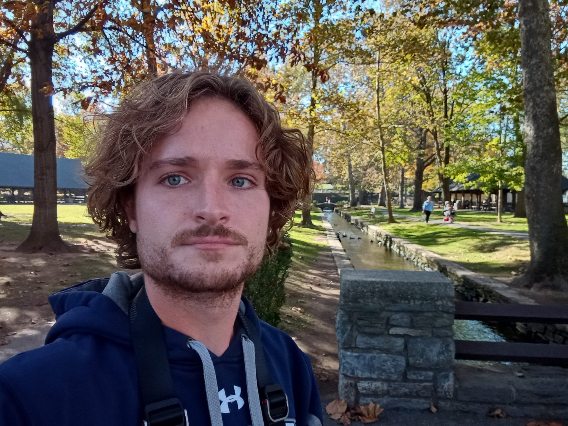 moto g pure standard selfie of a man with light curly hair and facial hair, wearing a t-shirt and hoodie, with trees behind him.
