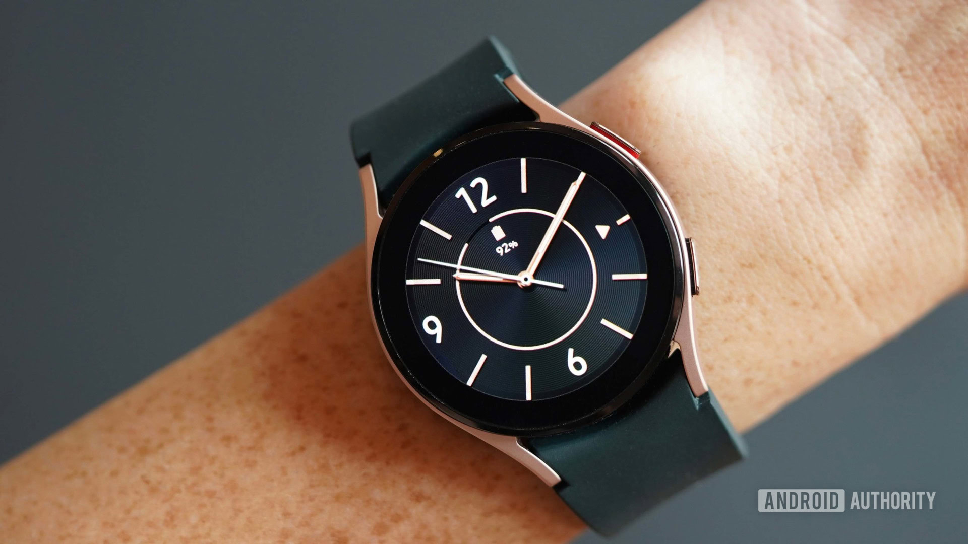 A Galaxy Watch 4 on a woman's wrist has an analog dial in black and rose gold.