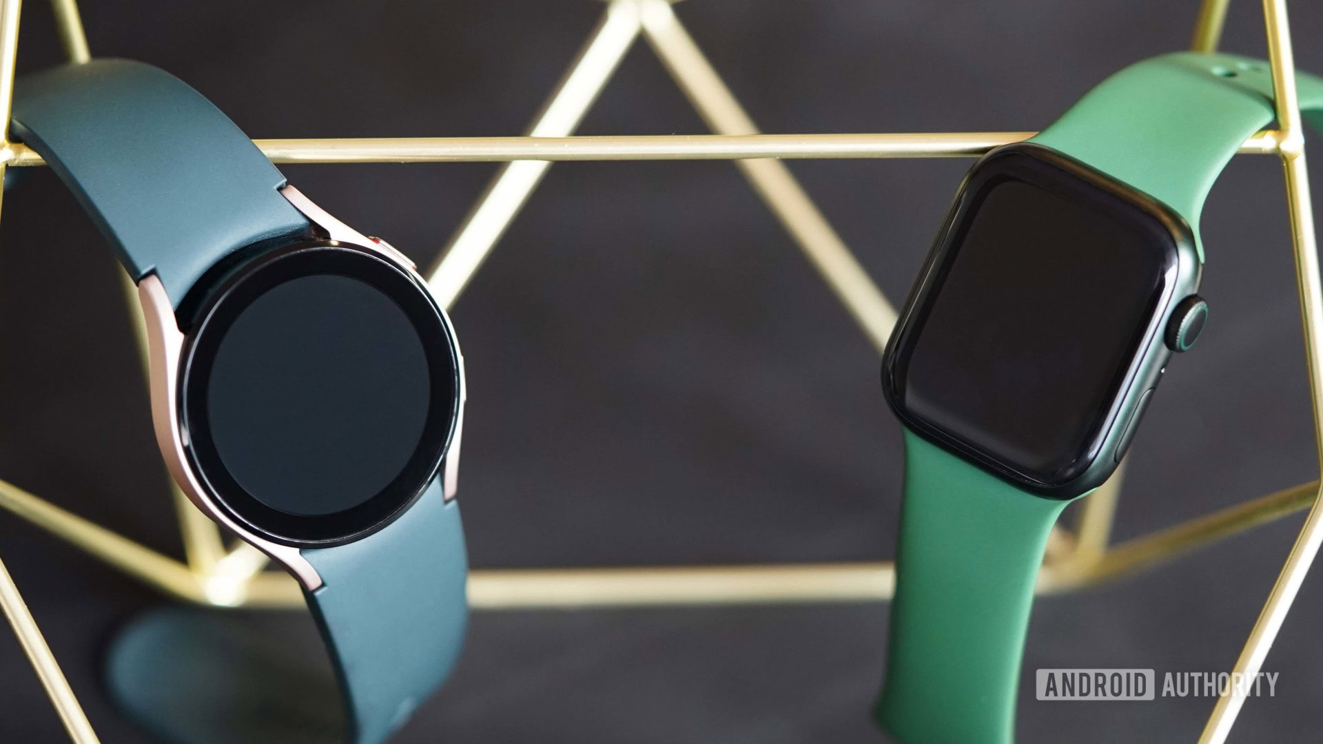 Um Galaxy Watch 4 e um Apple Watch 7 estão pendurados frente a frente em um suporte de medalha de ouro.