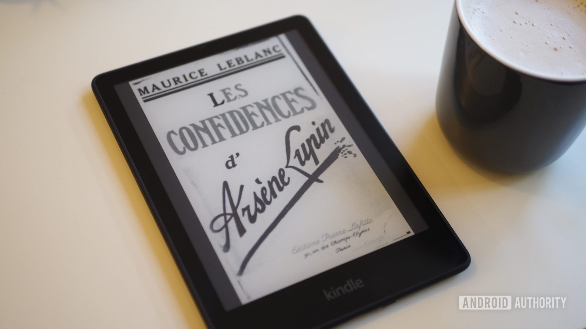 Amazon Kindle Paperwhite 2021 with the screen showing a book cover, on a table, next to a cup of coffee