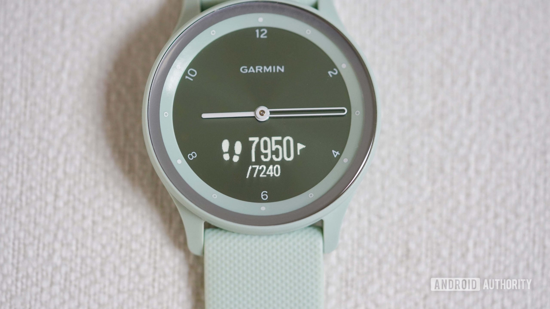 A Vivomove Sport rests on a white fabric surface with its hidden display activated and clock hands rotated to three and nine o clock.